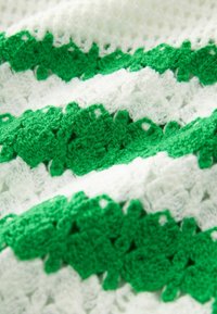 Horgolt zöld és fehér textil váltakozó csíkokkal. Texturált minták jellemzik, amelyek puha szálakat használnak, ezáltal réteges megjelenést kölcsönözve.