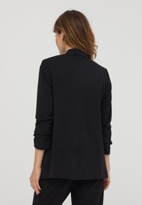 Blazer nero con una vestibilità su misura, maniche lunghe e colletto a punta. Il tessuto liscio e le linee pulite creano un design minimalista.