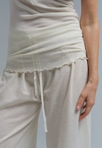 Ljusbeige loungewear-set som består av en lös topp med volangkant och byxor med justerbart snöre. Mjuk, lättviktig tyg med subtil textur.