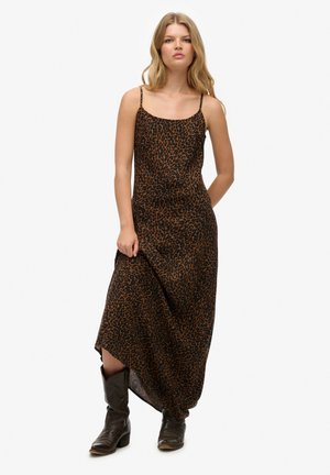 Robe maxi léopard en marron et noir, avec des bretelles fines et une silhouette fluide, accompagnée de bottes noires montantes jusqu'aux genoux.
