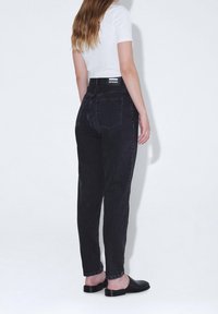 Svarta denimjeans med tapered passform, femficksdesign och logopatch på bakens midja. Stylad med en åtsittande vit skjorta och svarta skor.