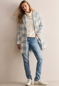 Randig kappa i mjukt tyg, ljusblå och vit mönster, parat med en krämfärgad polotröja och ljusblå jeans, avslutat med vita sneakers.