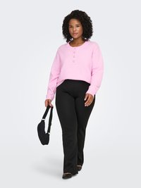 Pink cropped sweater with three buttons, paired with black flared pants. Model holds a small black bag, showcasing a casual look.