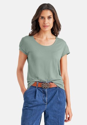 Helles grünes T-Shirt mit kurzen Ärmeln und rundem Halsausschnitt, lässig getragen zu blauen hochgeschnittenen Jeans und einem braunen Gürtel mit einer dekorativen Schnalle.