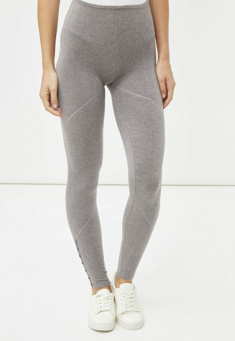 Leggings grises hechos de material suave, con una cintura alta, detalles de costura y acentos de botones a lo largo de la parte inferior de la pierna. Combinados con zapatillas blancas.
