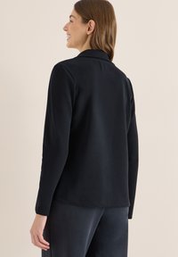 Zwart lang mouwen top met een gladde textuur, een op maat gemaakte kraag en subtiele stikdetails. De stof lijkt zacht en licht van gewicht.