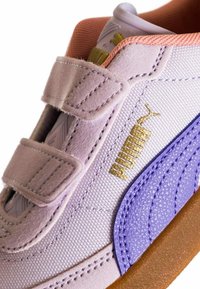 Sneaker di colore viola chiaro realizzata in materiali scamosciati e tessili, con una chiusura in velcro, logo dorato e un accento viola sul lato. Suola in gomma marrone.