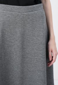 Grå jersey midiskjørt med en glatt tekstur, elastisk midje og en lett A-formet silhuett. Stoffet har et subtilt melert mønster.