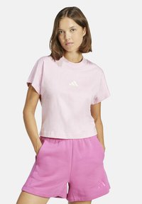 T-shirt in cotone rosa con maniche corte e scollatura rotonda, con logo Adidas bianco. Abbinato a pantaloni corti rosa coordinati.