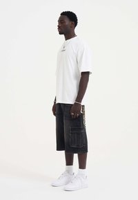 Hvid oversized t-shirt, sorte denim shorts med sidelomme og farverig broderi, hvide sneakers og ankelsokker.