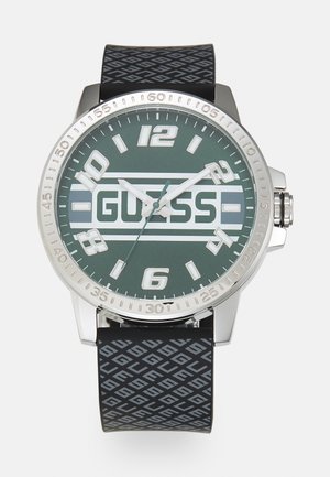 Quarzuhr mit einem Gehäuse aus silbernem Edelstahl und grünem Zifferblatt. Schwarzes Gummiband mit geometrischem Muster. Große Stundenmarkierungen.