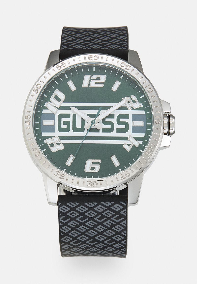 Reloj de cuarzo con caja de acero inoxidable plateada y esfera verde. Correa de goma negra con patrones geométricos. Grandes marcadores de hora.