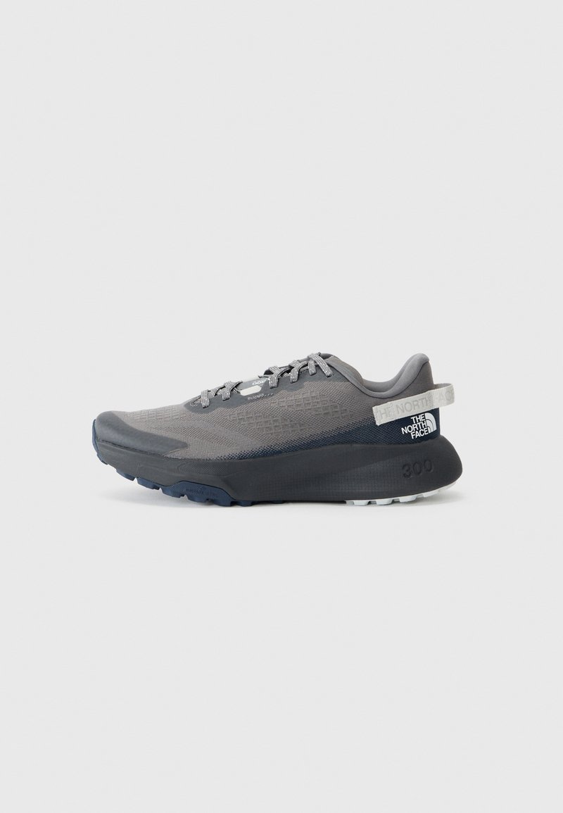 Chaussure de course grise avec une tige texturée, des lacets plats, une semelle robuste et une languette au talon arborant une marque. Accents dans des teintes plus sombres de gris.