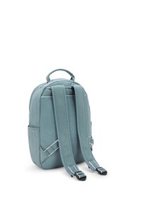 Zaino azzurro chiaro realizzato in tessuto con una superficie liscia. Presenta spallacci imbottiti, una maniglia superiore e cuciture bianche a contrasto sui bordi.