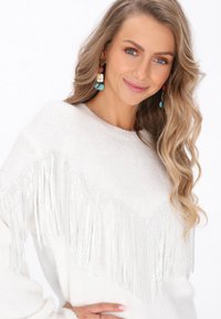 Maglione bianco a maglia con dettaglio frangiato a forma di V sulcollo, texture morbida e maniche lunghe.