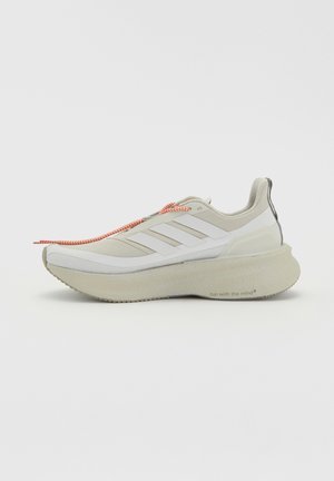 Beige og hvid løbesko med tyk sål, tre hvide striber på siden og orange snørebånd, vist fra den indvendige side.