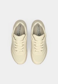 Αθλητικά παπούτσια σε κρεμ απόχρωση με υφή στο πάνω μέρος, διάτρητο σχέδιο και κορδόνια σε αντίθετο χρώμα. Φέρουν το λογότυπο "SKECHERS" στη γλώσσα.