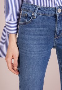 Jeans de mezclilla azul con un corte clásico, lavado claro, diseño de cinco bolsillos y cierre de botón, combinados con una camisa de mangas rayadas en azul y blanco.