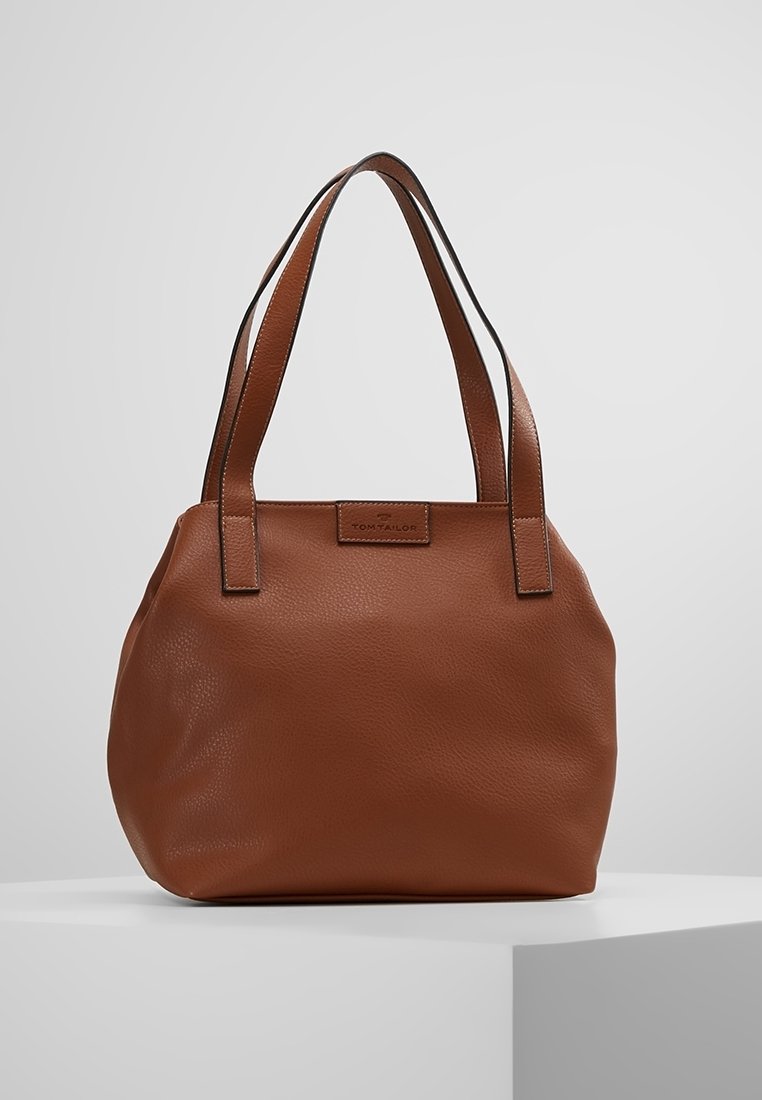 Sac cabas en cuir marron avec double anses et une petite étiquette de marque rectangulaire sur le centre avant supérieur.