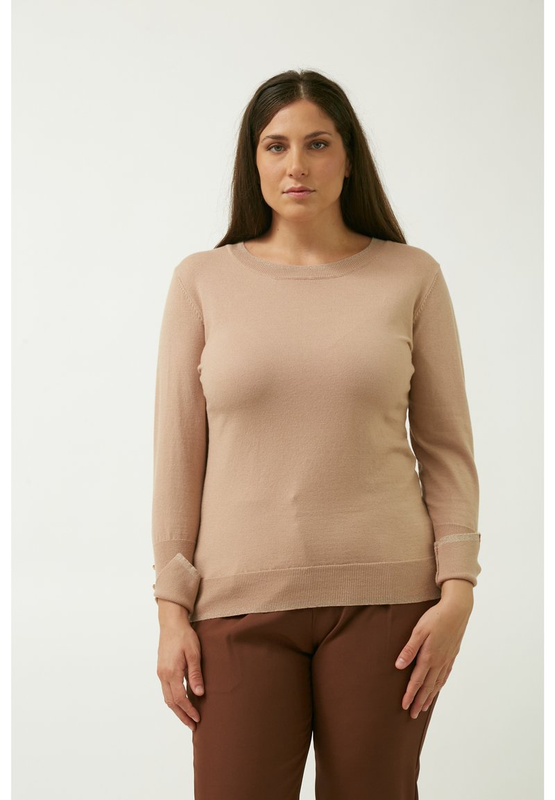 Lichtbeige gebreide trui met lange mouwen, geribbelde halslijn en boorden. Heeft een omgeslagen zoom bij de boorden en taille. Gecombineerd met een bruine broek.