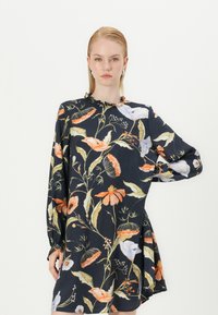 Vestido floral em azul marinho escuro com mangas longas, decote franzido e flores de várias cores. Tecido suave com um corte solto e barra rodada.