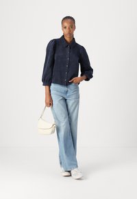 Navy corduroy button-up shirt with balloon sleeves, paired with light blue wide-leg jeans and a small white crossbody bag. White sneakers.