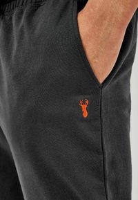 Zwarte katoenen joggingbroek met zijzakken, voorzien van een oranje hertlogo dat vlakbij de zak is geborduurd voor een kleurrijk accent.
