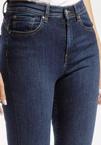 Ciemnoniebieskie dżinsy o dopasowanym kroju, z przednimi kieszeniami, subtelnymi przeszyciami i zamkiem błyskawicznym. Gładka, klasyczna faktura i sylwetka.