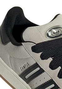 Baskets en daim gris avec des accents noirs, des lacets texturés et un badge logo rond sur la languette. "CAMPUS" est imprimé sur le côté.