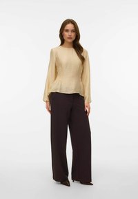 Top beige a maniche lunghe con texture e vita a peplo abbinato a pantaloni scuri a gamba larga. Scarpe con punta completano l'outfit.