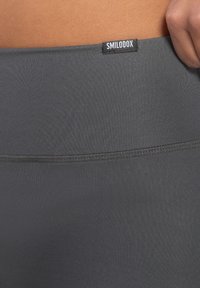 Leggings grigi in jersey elasticizzato realizzati in un tessuto morbido e liscio, con un ampio elastico in vita. Presentano un'etichetta nera con la scritta "SMILODOX" sulla vita.
