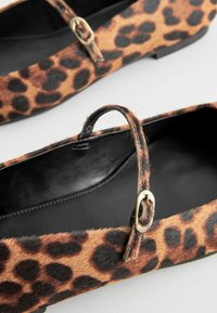 Chaussures plates à imprimé léopard en matériau doux avec un intérieur noir, dotées d'une sangle fine et d'accents en métal doré.
