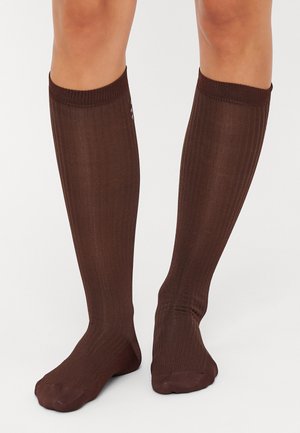 Bruna knähöga strumpor gjorda av ribbat tyg med en slät yta. De har en förstärkt tå och ett bekvämt elastiskt band upptill.
