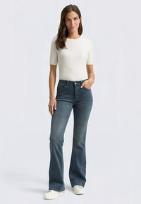 Liemenėlę pabrėžianti balta trumpomis rankovėmis viršutinė dalis, derinta su tamsiai mėlynais platėjančiais džinsais, turinčiais klasikinį penkių kišenių dizainą ir švelnų išblukimą.