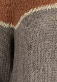 Suéter de punto con tonos tierra de óxido, marrón y gris. Tejido texturizado con costuras en crema contrastantes a lo largo de las costuras.