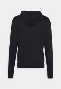 Schwarzer Kapuzenpullover mit langen Ärmeln, gerippten Bündchen und einem kleinen Logodetail am unteren linken Saum. Glatte Stofftextur.