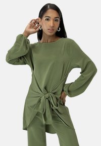 Olivgrünes Langarmshirt mit lockerem Schnitt, einem Knoten am Taillenbund und aus weichem, glattem Stoff gefertigt, mit einem entspannten Rundhalsausschnitt.