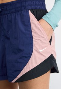 Námornícke a ružové bežecké šortky s čiernym akcentom, elastickým pásom, bočnými vreckami a malým bielym logom Nike vpredu.