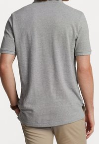 Šedé polo tričko vyrobené z texturované látky s límečkem a krátkými rukávy. Zadní pohled ukazuje jednoduchý, čistý design bez ozdob.