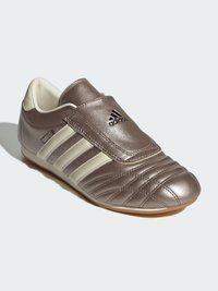 Brown leather soccer shoes with a rounded toe, elastic strap, three white side stripes, and padded texture. Features embossed detailing.