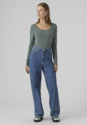 Langsleeve, olijfgroene top en high-waisted, straight-leg blauwe denim jeans met zijzakken en metalen knopdetails.