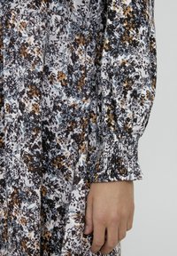 Rochie cu model floral, având un fundal alb cu flori negre, maronii și albastre. Mâneci strânse cu elastic la tiv.
