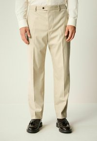 Beige Schnitt-Hose mit geradem Schnitt, Frontfalten und einem Reißverschluss. Verfügt über Gürtelschlaufen und einen einzelnen Knopfverschluss.