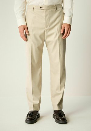 Pantalones beige ajustados con corte recto, pliegues frontales y cremallera. Cuenta con trabillas para cinturón y un cierre de un solo botón.