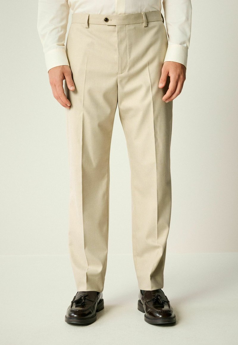 Beige Schnitt-Hose mit geradem Schnitt, Frontfalten und einem Reißverschluss. Verfügt über Gürtelschlaufen und einen einzelnen Knopfverschluss.