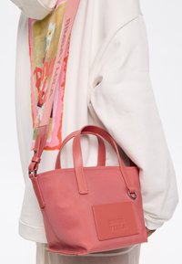 Borsa sintetica rosa con due manici superiori e una tracolla rimovibile. Presenta dettagli cuciti e una patch con logo sulla parte anteriore.