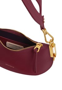 Borsa in pelle bordeaux con zip e accessori dorati. Presenta una forma curva, una superficie testurizzata e una chiusura sicura a scatto.