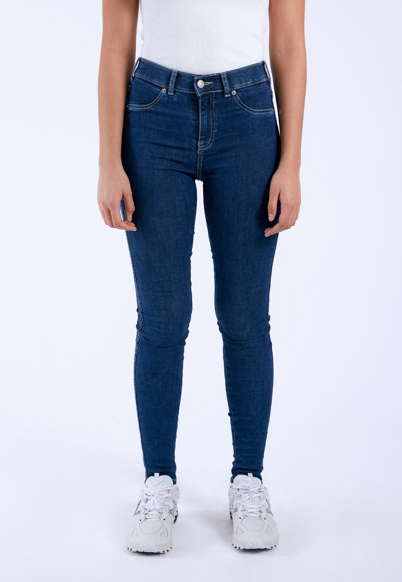 Dark blue denim jeans with a high waist, slim fit, and front pockets. Features a zip fly and contrasting stitching along the seams.