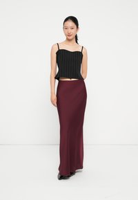 Fekete csíkos crop top szív alakú dekoltázzsal, hosszú bordó sima szoknyával párosítva. A modell egy sima fehér háttér előtt áll.