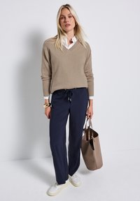 Beige v-neck sweater, navy drawstring pants, white sneakers, and a taupe tote bag. Smooth textures; casual fit; minimalistic design.